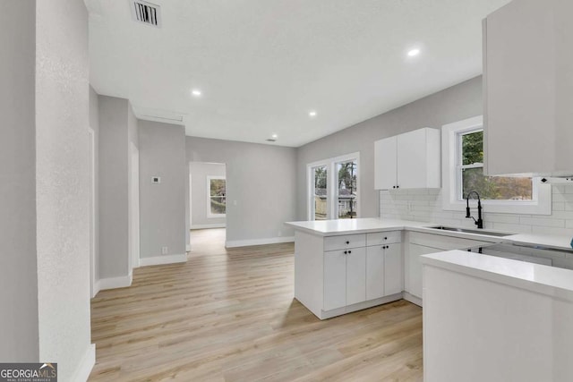 kitchen with sink, tasteful backsplash, kitchen peninsula, light hardwood / wood-style floors, and white cabinets