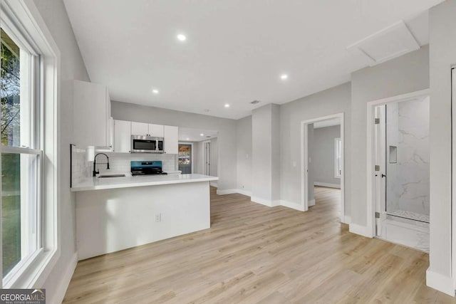 kitchen featuring black stove, sink, kitchen peninsula, light hardwood / wood-style floors, and white cabinets