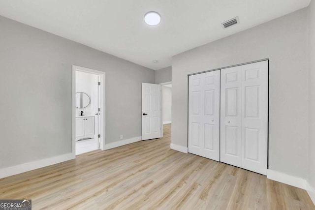 unfurnished bedroom featuring ensuite bath, a closet, and light hardwood / wood-style flooring