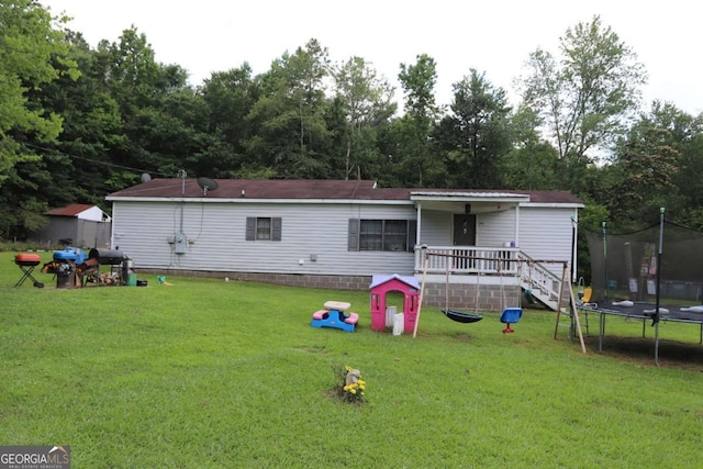 rear view of property with a trampoline and a yard