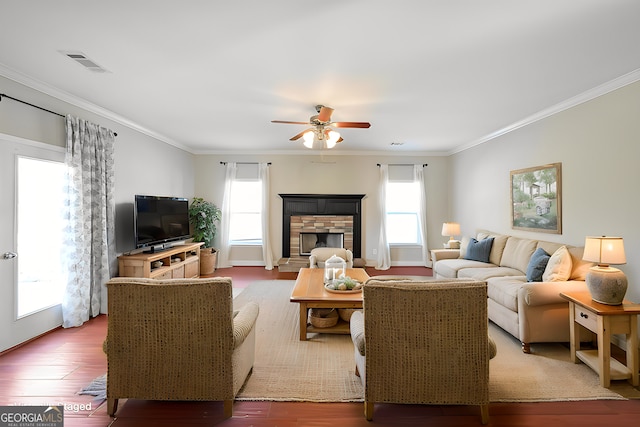 living room featuring visible vents, ornamental molding, a ceiling fan, a stone fireplace, and wood finished floors