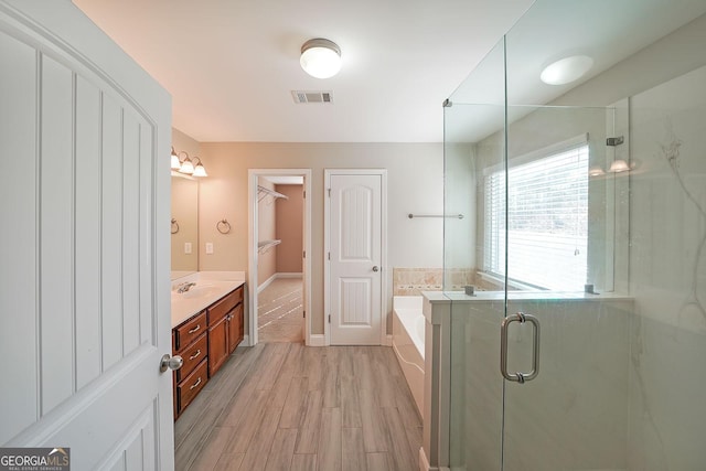 bathroom with a stall shower, visible vents, wood finished floors, a garden tub, and vanity