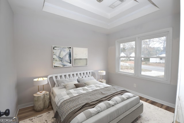 bedroom with a raised ceiling, crown molding, and hardwood / wood-style flooring