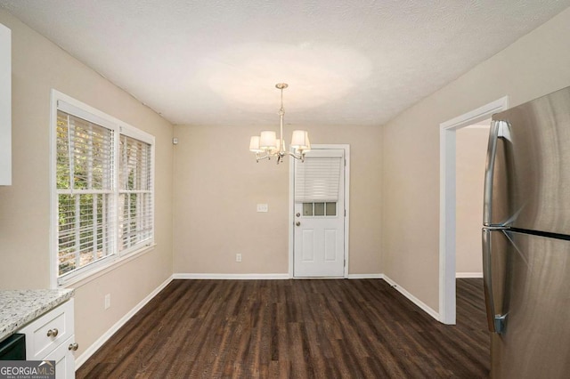 unfurnished dining area featuring a chandelier, a textured ceiling, and dark hardwood / wood-style flooring