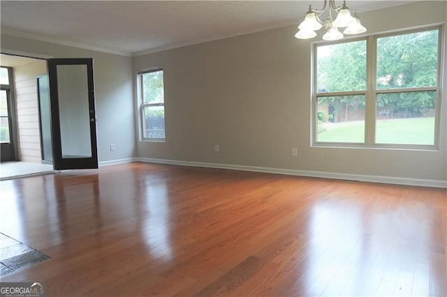 spare room with a notable chandelier, wood-type flooring, and ornamental molding