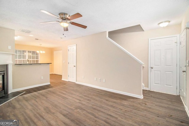 unfurnished living room featuring a textured ceiling, ceiling fan with notable chandelier, and dark wood-type flooring