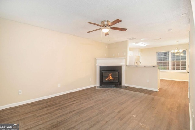 unfurnished living room featuring wood-type flooring, ceiling fan with notable chandelier, and a textured ceiling