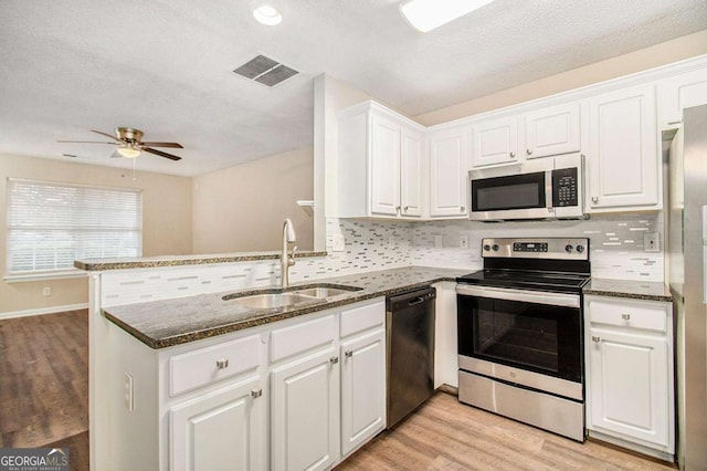 kitchen with kitchen peninsula, appliances with stainless steel finishes, sink, light hardwood / wood-style flooring, and white cabinets