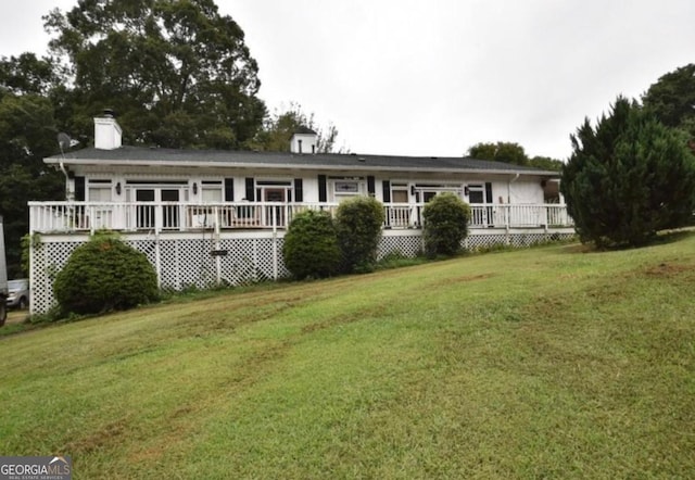 view of front of home featuring a deck, a chimney, and a front yard