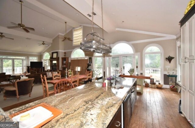 kitchen featuring ceiling fan, ornamental molding, light stone counters, hardwood / wood-style flooring, and high vaulted ceiling