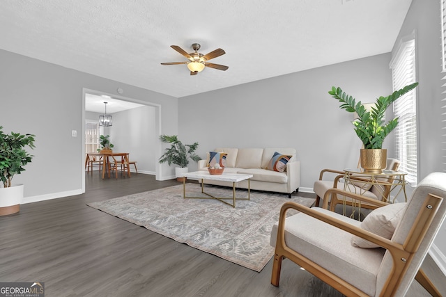 living room with ceiling fan with notable chandelier, dark wood-type flooring, and a healthy amount of sunlight