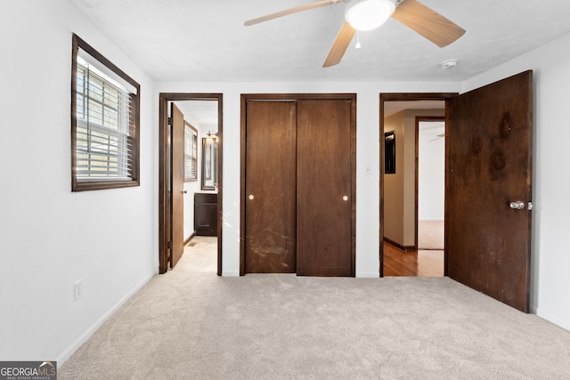 unfurnished bedroom with baseboards, ceiling fan, light colored carpet, ensuite bathroom, and a closet