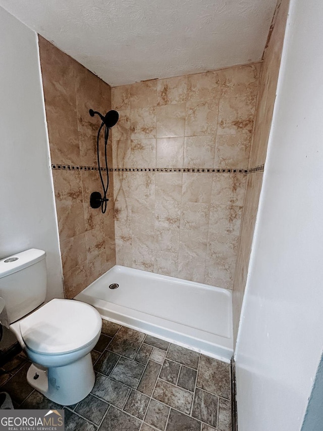 bathroom with toilet, a tile shower, and a textured ceiling