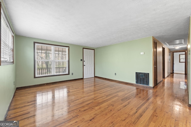 unfurnished living room with baseboards, visible vents, attic access, hardwood / wood-style flooring, and a textured ceiling