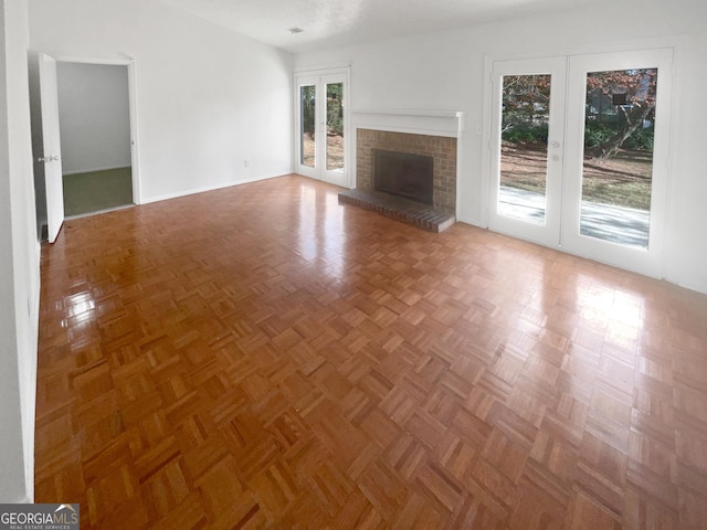 unfurnished living room with parquet flooring, french doors, and a brick fireplace