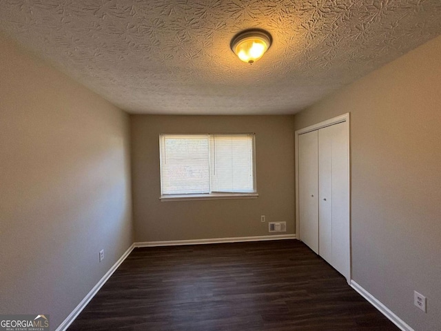 unfurnished bedroom with a closet, a textured ceiling, and dark hardwood / wood-style floors