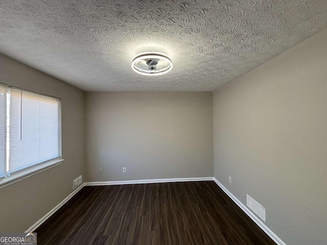 spare room featuring a textured ceiling and dark hardwood / wood-style flooring