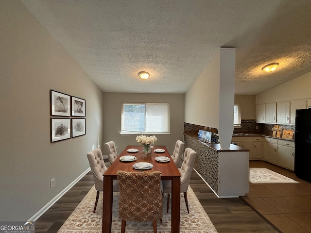 dining space featuring a textured ceiling, dark hardwood / wood-style flooring, vaulted ceiling, and sink