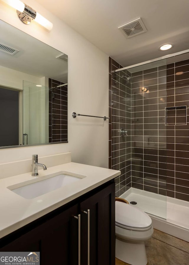 bathroom featuring tile patterned flooring, vanity, toilet, and a tile shower