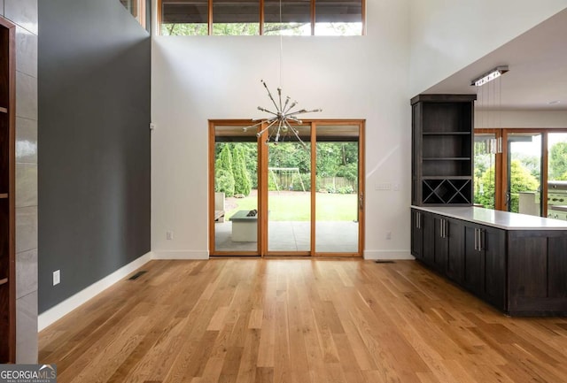 interior space with light hardwood / wood-style flooring, a towering ceiling, and a chandelier