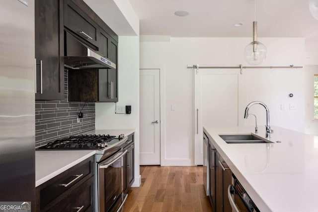 kitchen featuring backsplash, sink, light hardwood / wood-style flooring, appliances with stainless steel finishes, and decorative light fixtures