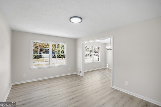 spare room featuring light hardwood / wood-style floors, a textured ceiling, and a chandelier