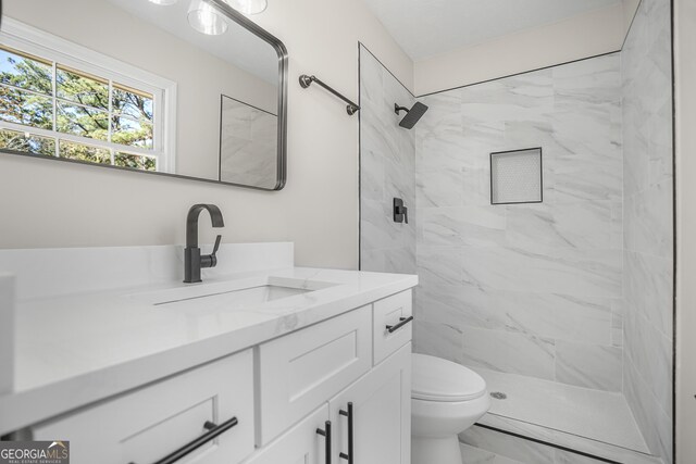 bathroom with tiled shower, vanity, and toilet