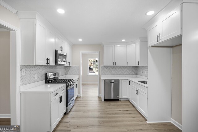 kitchen featuring sink, backsplash, appliances with stainless steel finishes, white cabinets, and light wood-type flooring