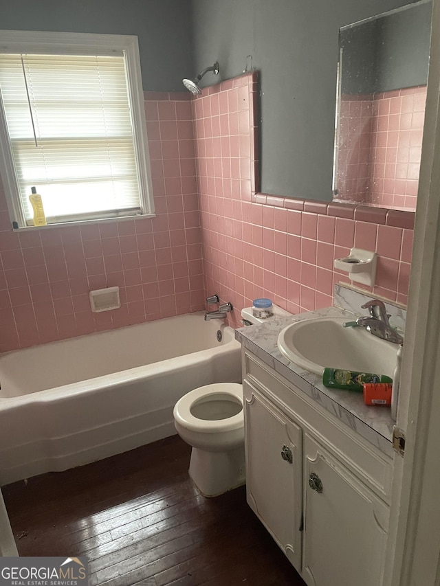 full bathroom featuring hardwood / wood-style floors, tiled shower / bath combo, vanity, tile walls, and toilet