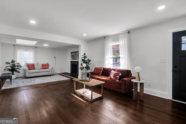 living room with a skylight, a fireplace, and dark wood-type flooring