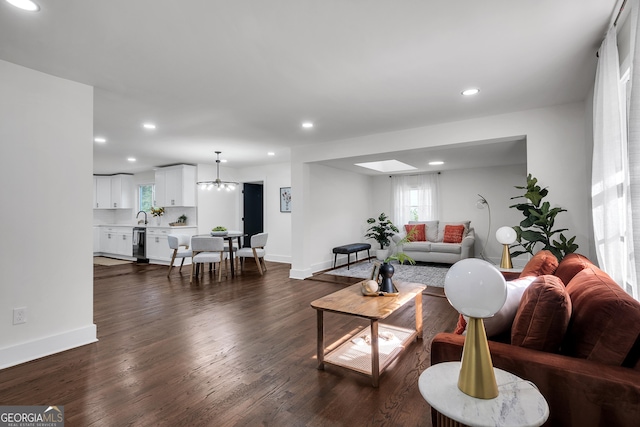 living room featuring a skylight, sink, a chandelier, and dark hardwood / wood-style floors