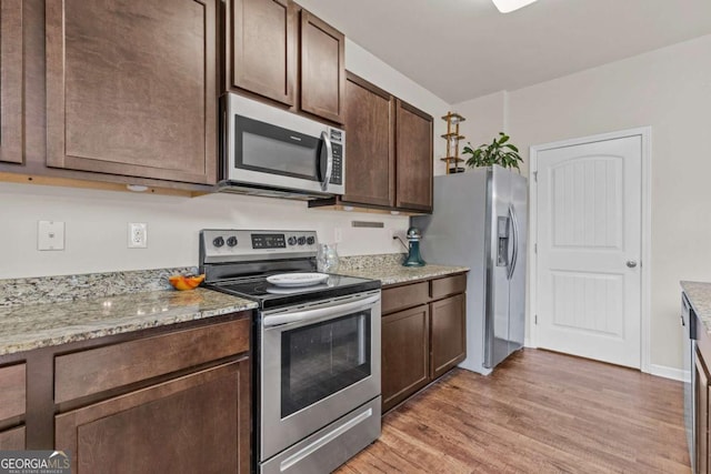 kitchen with dark brown cabinets, light wood-type flooring, stainless steel appliances, and light stone counters