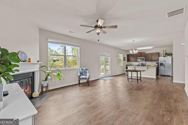 living room featuring a fireplace, wood-type flooring, and ceiling fan with notable chandelier