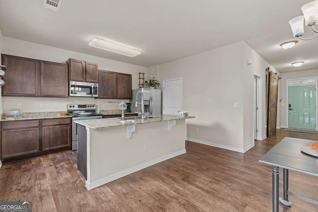 kitchen with light stone countertops, appliances with stainless steel finishes, dark hardwood / wood-style flooring, a center island with sink, and a breakfast bar area