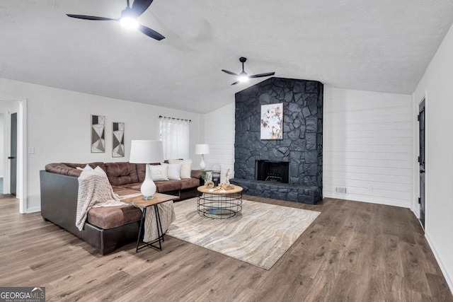 living room featuring vaulted ceiling, ceiling fan, wooden walls, hardwood / wood-style flooring, and a fireplace