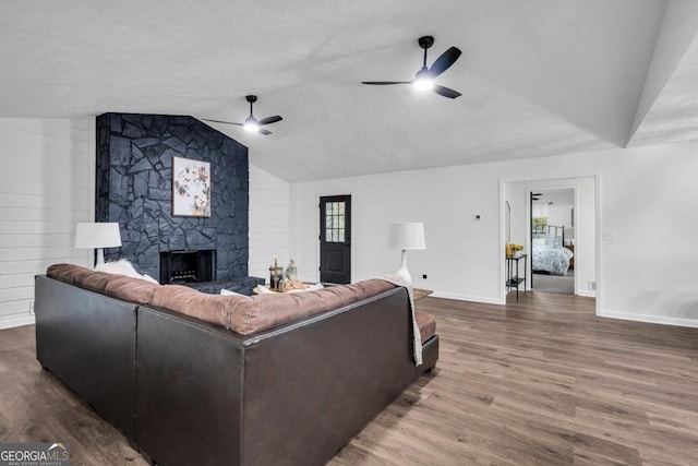 living room with a textured ceiling, ceiling fan, wood-type flooring, a stone fireplace, and lofted ceiling