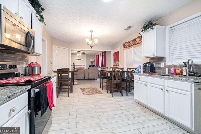 kitchen with white cabinetry, hanging light fixtures, a textured ceiling, ceiling fan with notable chandelier, and appliances with stainless steel finishes