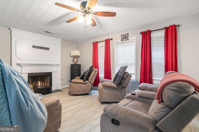 living room with a textured ceiling, light wood-type flooring, and ceiling fan