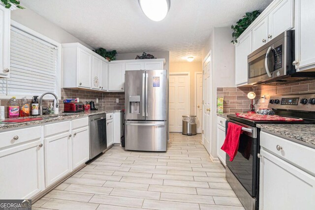 kitchen with light stone countertops, a textured ceiling, light wood-type flooring, appliances with stainless steel finishes, and white cabinetry