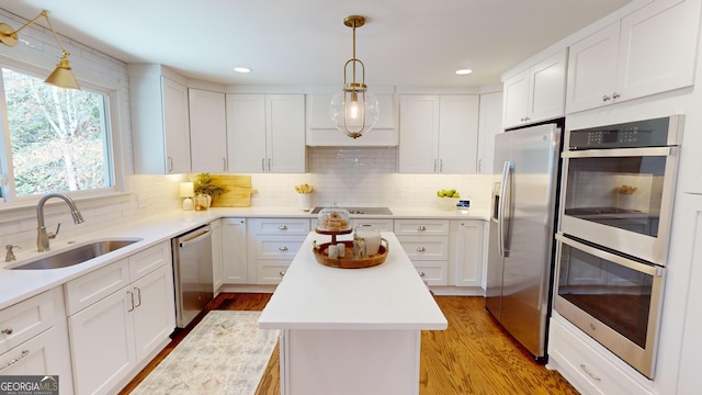 kitchen with appliances with stainless steel finishes, sink, white cabinets, a center island, and light hardwood / wood-style floors