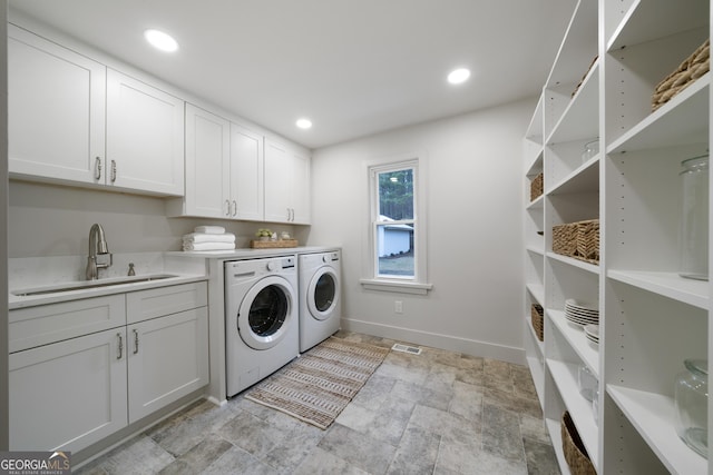 clothes washing area with washer and dryer, cabinets, and sink