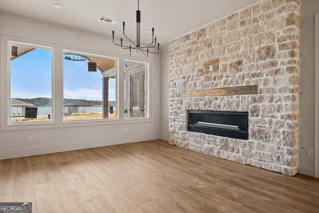 unfurnished dining area with hardwood / wood-style floors, a stone fireplace, a water view, and a chandelier