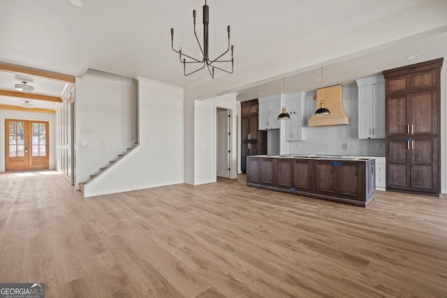 kitchen with french doors, custom exhaust hood, dark brown cabinetry, decorative light fixtures, and light hardwood / wood-style flooring