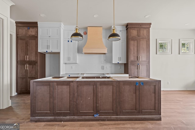 kitchen featuring dark brown cabinetry, hanging light fixtures, hardwood / wood-style floors, an island with sink, and custom range hood