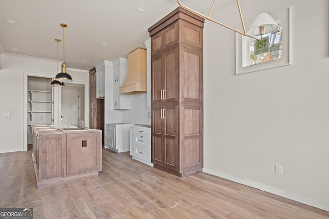 kitchen with pendant lighting, a center island, white cabinets, light wood-type flooring, and custom range hood