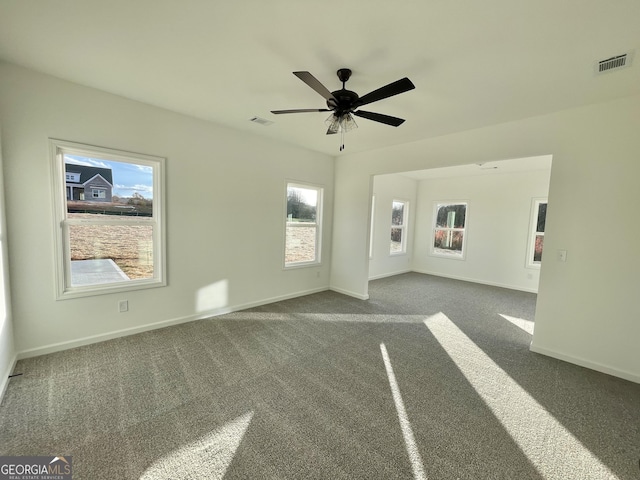 unfurnished living room featuring dark carpet, a wealth of natural light, and ceiling fan