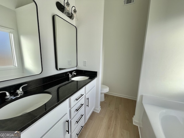 bathroom with a tub to relax in, hardwood / wood-style floors, vanity, and toilet