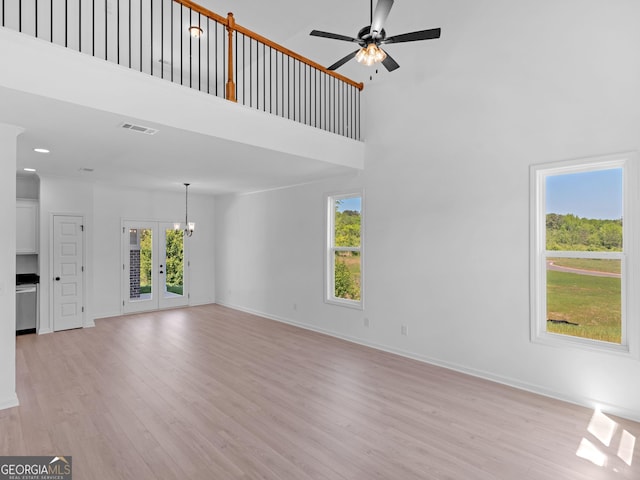 1215 White Oak Way, Griffin, GA 30224 - unfurnished living room with light wood-style flooring, a ceiling fan, baseboards, a towering ceiling, and a chandelier