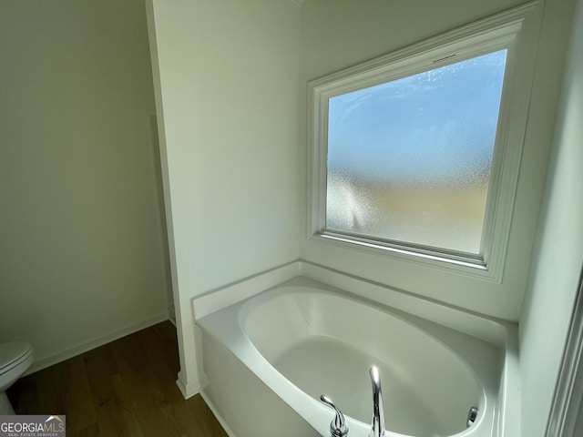 bathroom featuring hardwood / wood-style flooring, toilet, and a tub to relax in