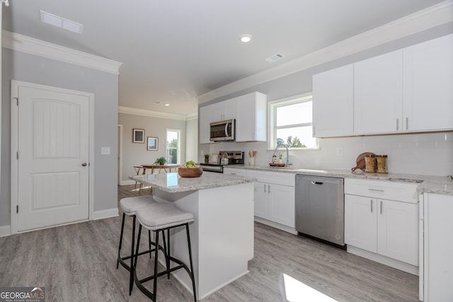 kitchen with stainless steel appliances, a kitchen island, visible vents, a kitchen bar, and crown molding